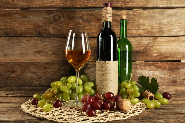Witte en rode druif met fles wijn op houten achtergrond — Stockfoto