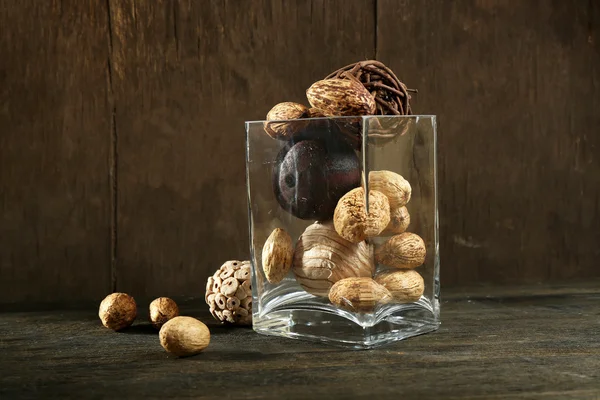 Composition of nuts and wooden balls in glass on resembling wood table — Stock Photo, Image