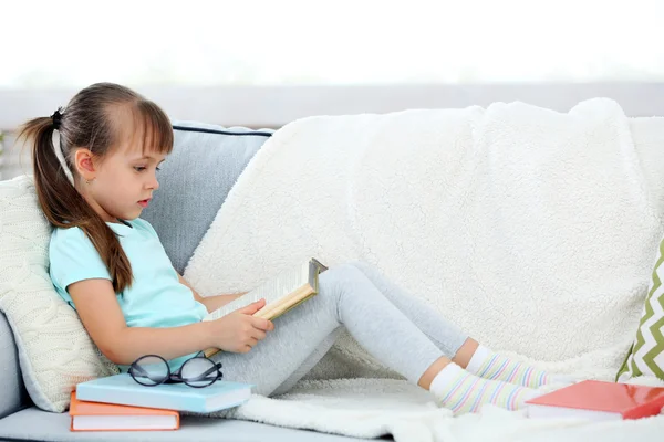 Petite fille assise sur un canapé avec un livre — Photo