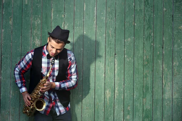 Hombre guapo toca el saxofón sobre fondo de madera verde — Foto de Stock