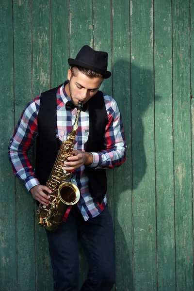 Hombre guapo toca el saxofón sobre fondo de madera verde — Foto de Stock