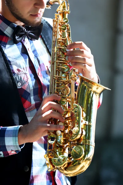 Młody człowiek gra saksofon na tle miejskich, zamyka się — Zdjęcie stockowe