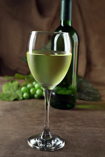 Copo de vinho branco contra garrafa e uva na mesa de madeira — Fotografia de Stock