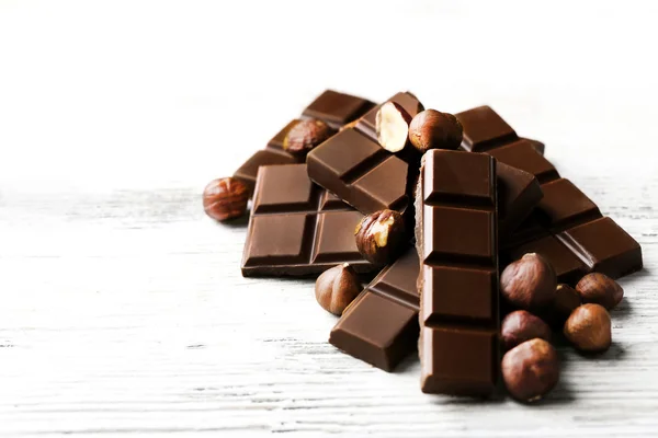 Pezzi di cioccolato con noci su sfondo di legno colore — Foto Stock