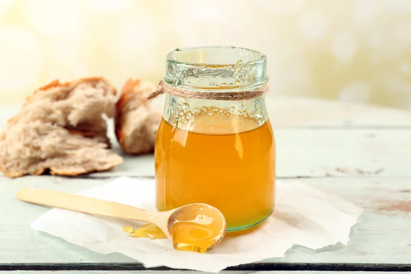 Frasco de mel com colher de madeira no fundo claro — Fotografia de Stock