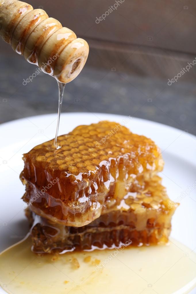 Honey dripping on honeycombs on plate on wooden background