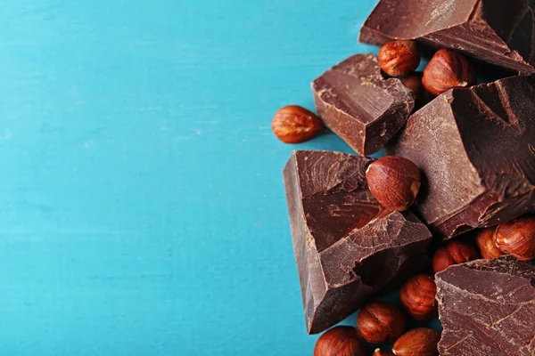 Black chocolate pieces with nuts on color wooden background — Stock Photo, Image