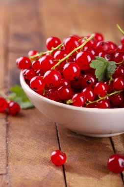 Ahşap masa üzerinde kase taze kırmızı kuş üzümü yakın çekim