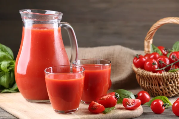 Pot plein et verres de jus de tomate avec légumes sur table en bois close up — Photo