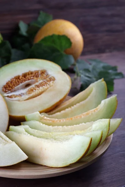 Segmenten van rijpe meloenen met groene bladeren op tafel close-up — Stockfoto