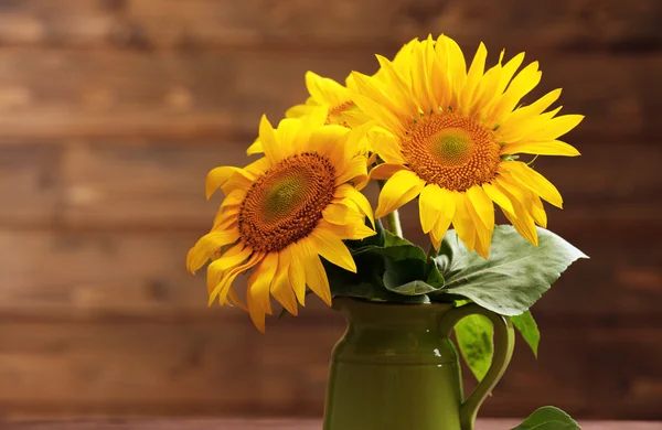 Schöne helle Sonnenblumen im Krug auf hölzernem Hintergrund — Stockfoto