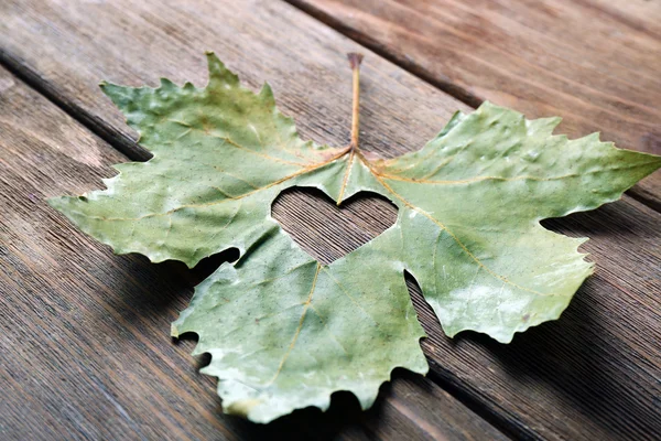 Feuille d'automne séchée avec coeur découpé sur fond en bois — Photo