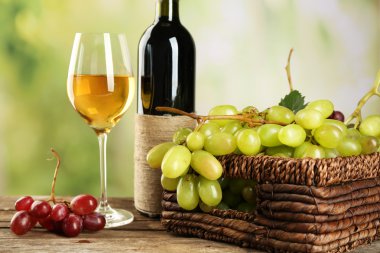 Ahşap masa üzerinde şarap şişesi ile sepette beyaz üzüm demet