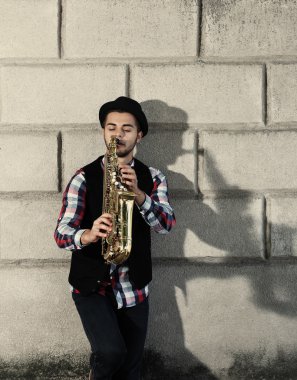 Sax tuğla duvar arka plan üzerinde olan yakışıklı genç adam