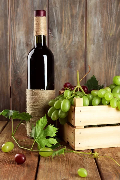Uva branca e vermelha em caixa com garrafa de vinho em fundo de madeira — Fotografia de Stock