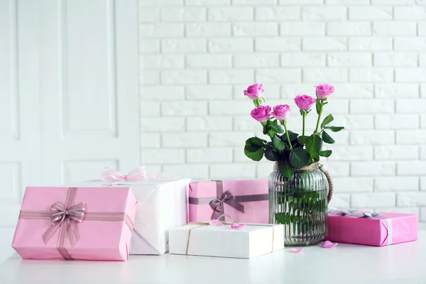 Composition of colourful gift boxes and flowers in glass on white table in front of brick wall background