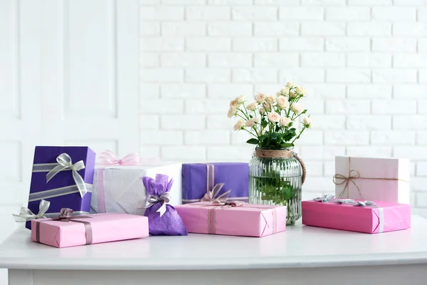 Composition de boîtes-cadeaux colorées et fleurs en verre sur table blanche devant le fond du mur de briques — Photo