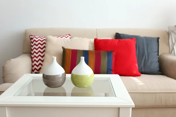 Beiges Sofa mit schönen Kissen und dekorativen Vasen auf dem Tisch davor im Zimmer — Stockfoto