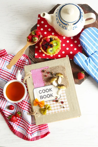 Украшенная поваренная книга с чайником и вкусным тортом на столе — стоковое фото