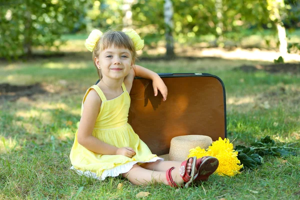 Little girl with suitcase on grass in park — Stock Photo, Image