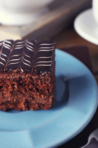 Zoete chocolade taart op blauw bord met kopje thee op bruin katoen servetring, close-up — Stockfoto