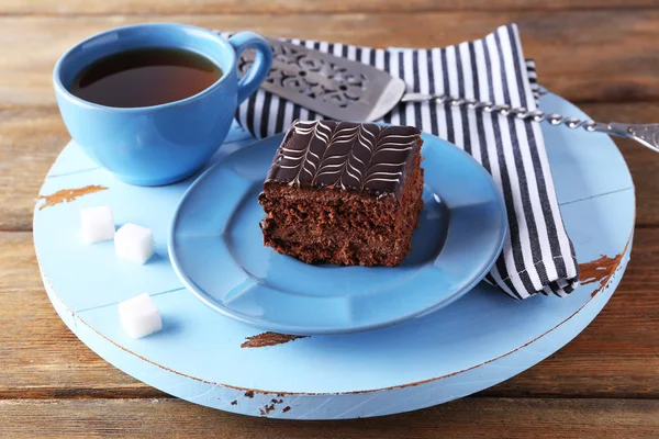 Pastel de chocolate dulce en plato azul con taza de té en mesa de madera —  Fotos de Stock
