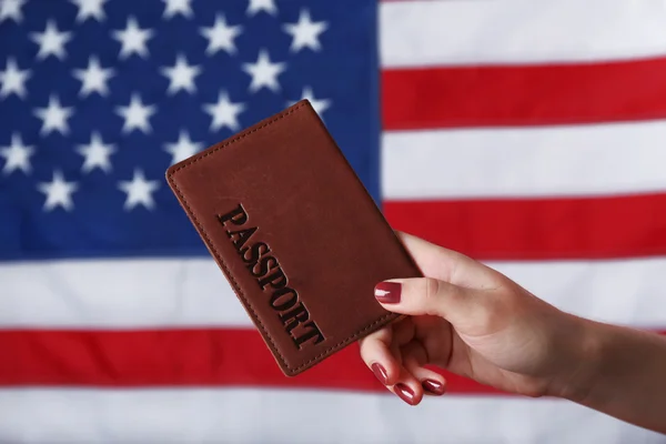 Una mano che tiene il passaporto sullo sfondo della bandiera americana — Foto Stock