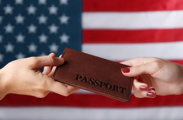 Uma mão dando o passaporte a outra no fundo da bandeira americana — Fotografia de Stock