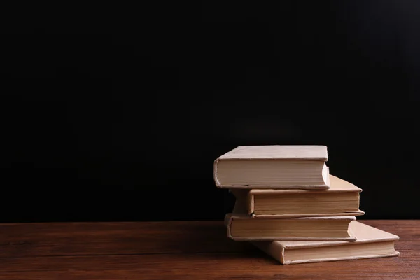 Stapel gesloten oude boeken op houten tafel tegen zwarte achtergrond — Stockfoto