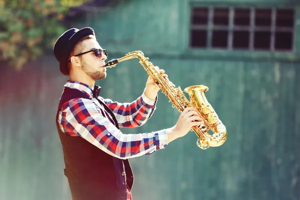 Jovem tocando saxofone fora perto da parede velha — Fotografia de Stock