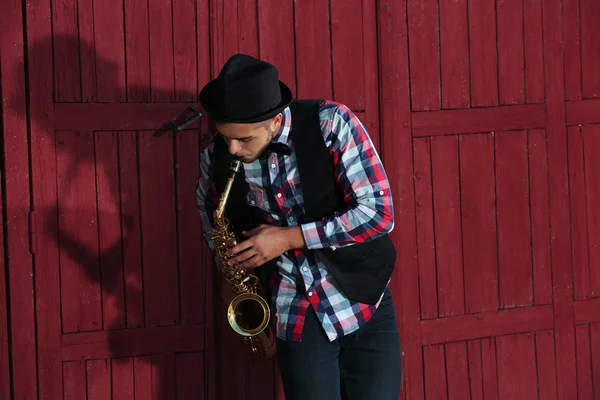 Joven tocando el saxofón afuera cerca de la vieja pared — Foto de Stock