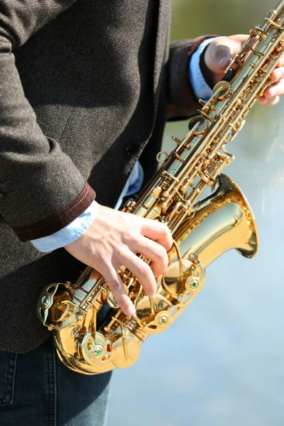 Joven tocando el saxofón a orillas del río — Foto de Stock