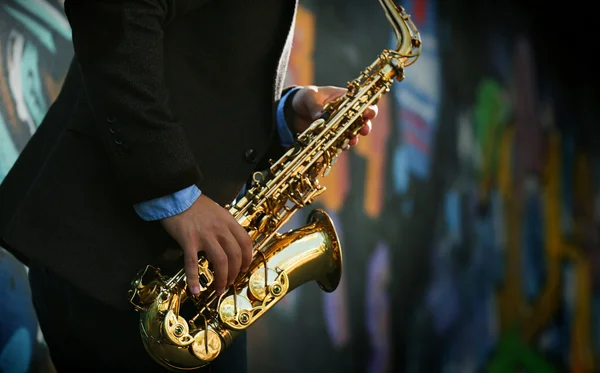 Jovem com saxofone fora perto da parede pintada velha — Fotografia de Stock