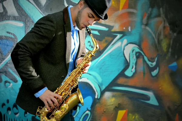 Joven con saxofón afuera cerca de la vieja pared pintada —  Fotos de Stock