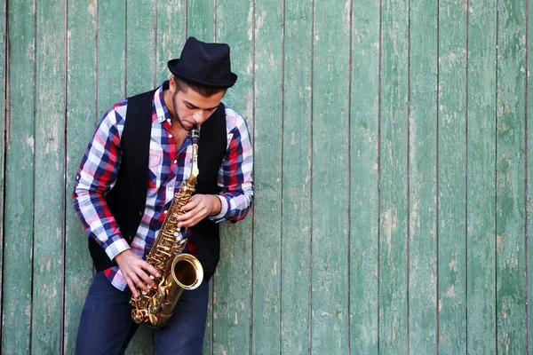 El músico toca el saxofón sobre fondo de madera verde —  Fotos de Stock
