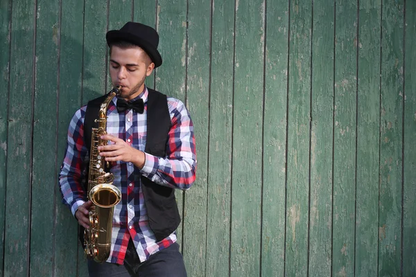 Hombre guapo toca el saxofón sobre fondo de madera verde —  Fotos de Stock