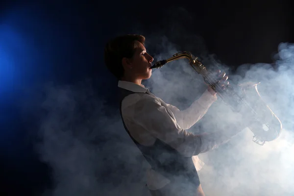 Mujer atractiva toca el saxofón sobre fondo oscuro en el humo —  Fotos de Stock