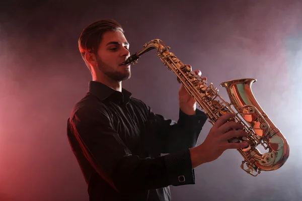Joven profesional toca saxo en humo rojo — Foto de Stock