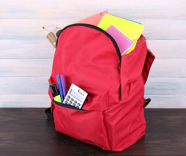 Красная сумка со школьным оборудованием на деревянном фоне — стоковое фото