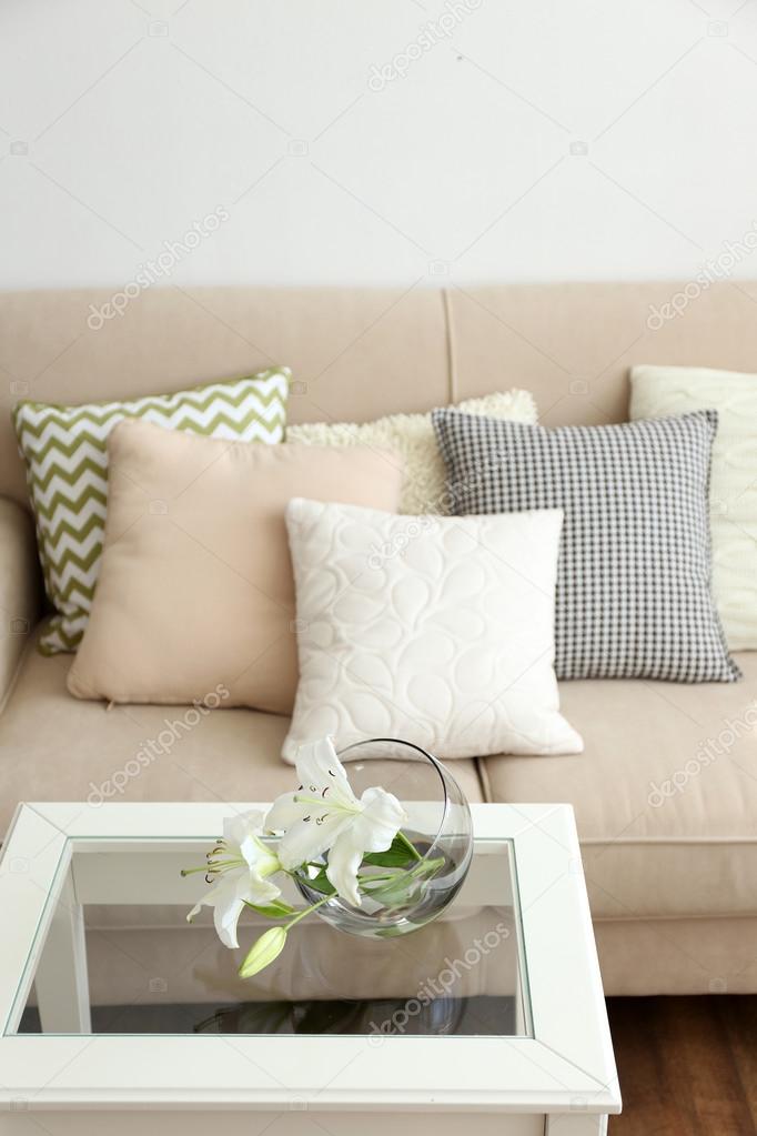 Pastel color sofa with beautiful pillows and vase with flowers on the
