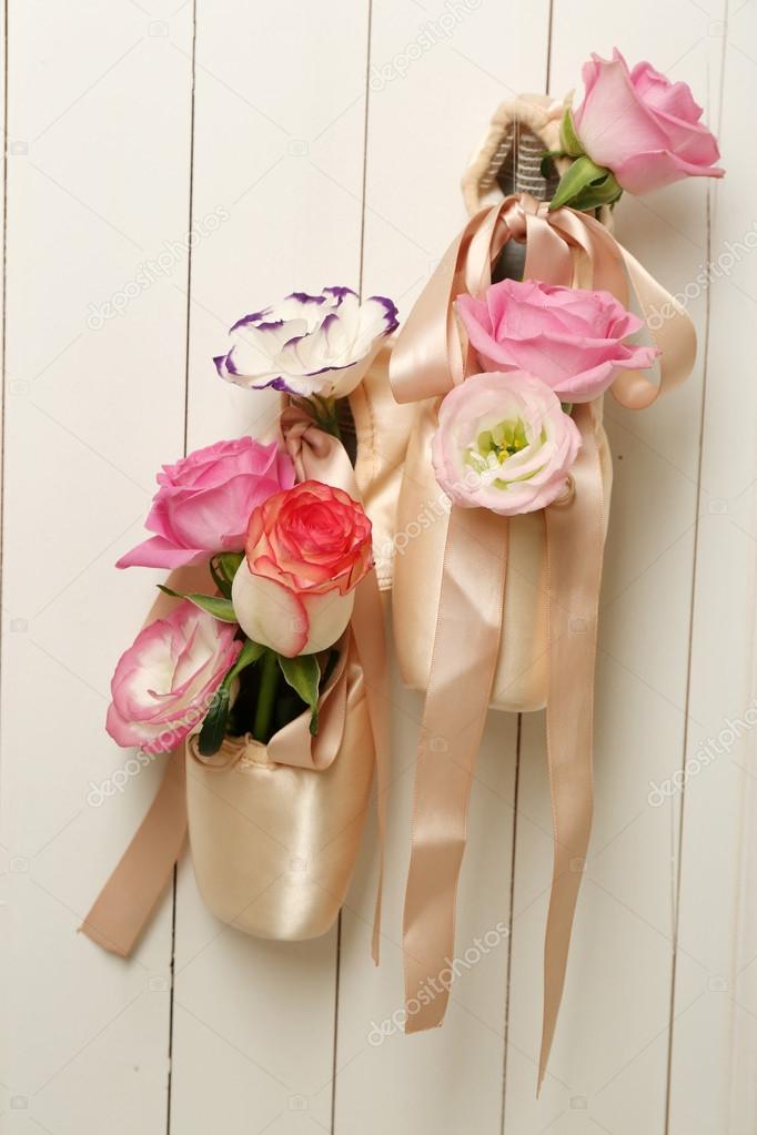 Decorated ballet shoes with roses in it hanging on light wooden wall background
