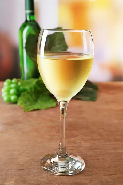 Bicchiere di vino bianco con bottiglia e uva su tavolo di legno su sfondo sfocato — Foto Stock