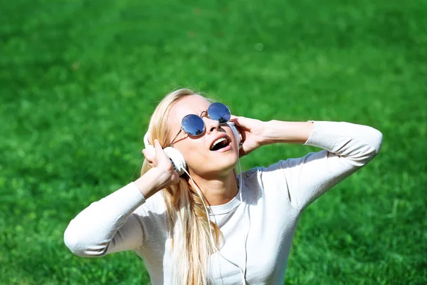 Młoda kobieta z słuchawki i smartphone słuchanie muzyki na trawie — Zdjęcie stockowe