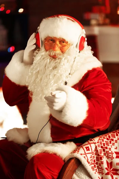 Santa Claus zitten met koptelefoon zitten in comfortabele schommelstoel thuis — Stockfoto