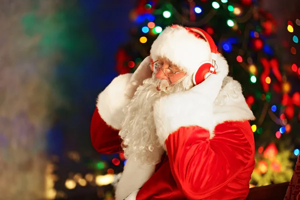 Papai Noel sentado com fones de ouvido sentado em cadeira de balanço confortável em casa — Fotografia de Stock