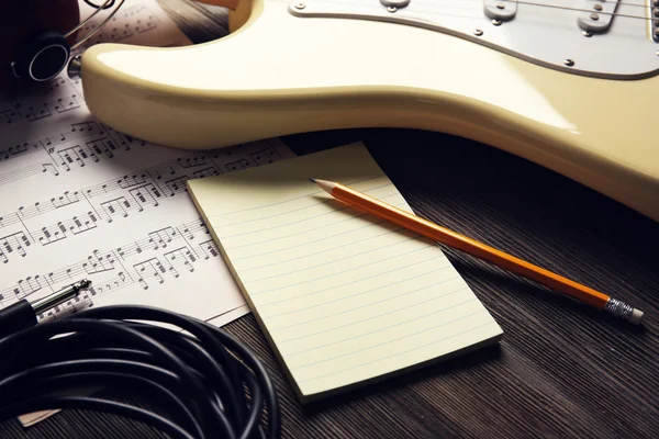 Chitarra elettrica con note musicali, matita e spartito su fondo legno — Foto Stock