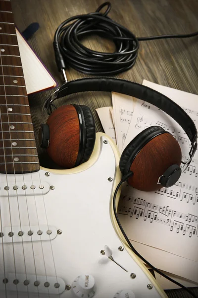 Electric guitar with headphones, musical notes and note book on wooden background — Stock Photo, Image