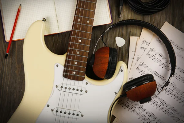 Electric guitar with headphones, musical notes and note book on wooden background — Stock Photo, Image