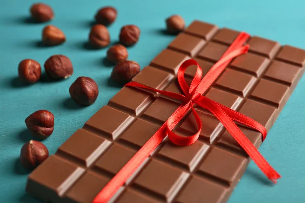 Barra de chocolate de leite com arco vermelho na cor de fundo de madeira — Fotografia de Stock