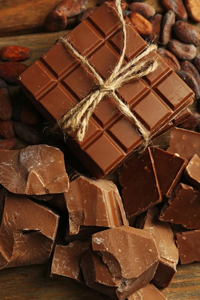 Pezzi di cioccolato, trucioli e fave di cacao su sfondo di legno di colore — Foto Stock